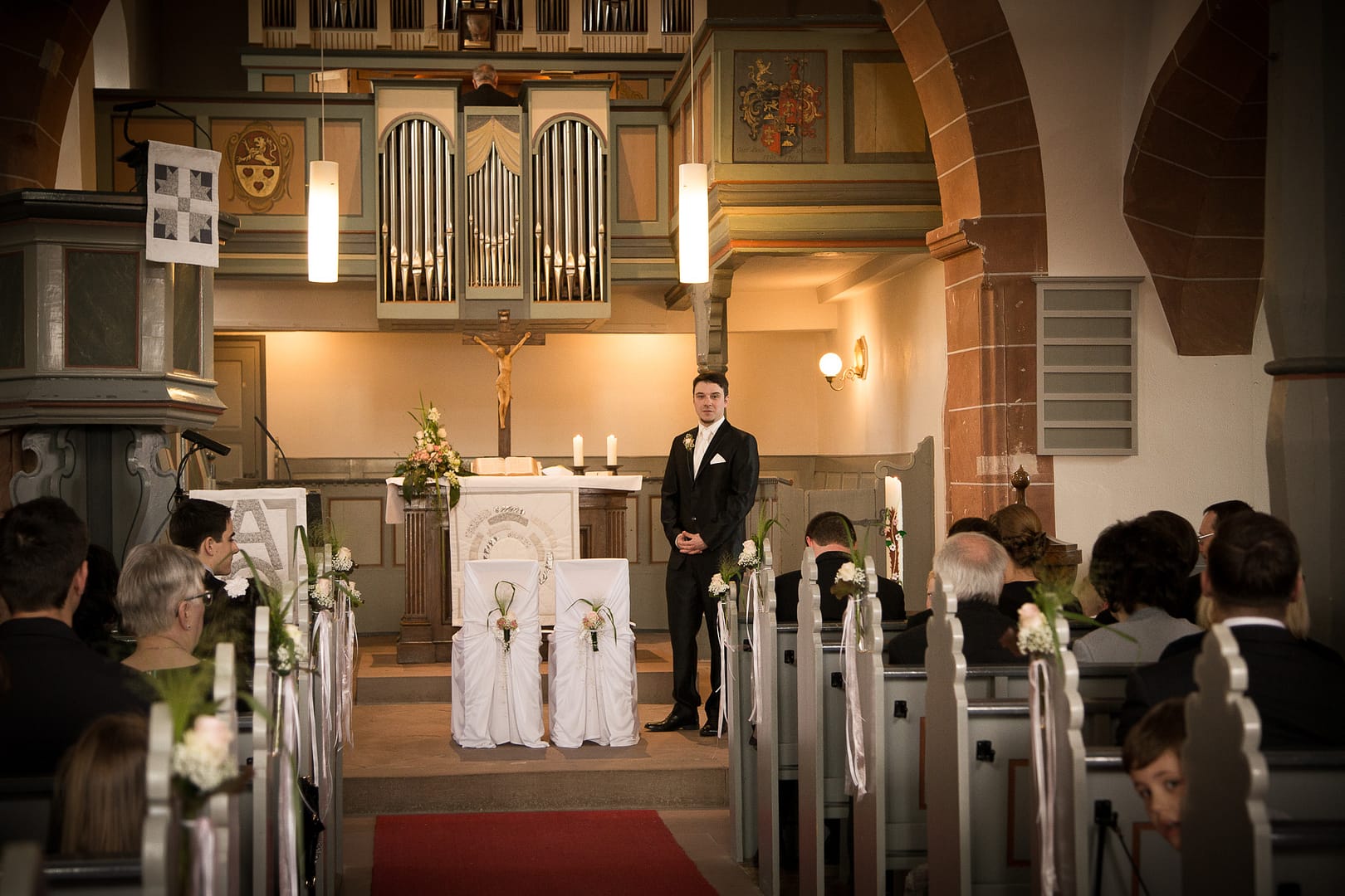 Der Bräutigam steht im Kirchensaal neben dem Altar und wartet darauf seine Braut zu sehen.
