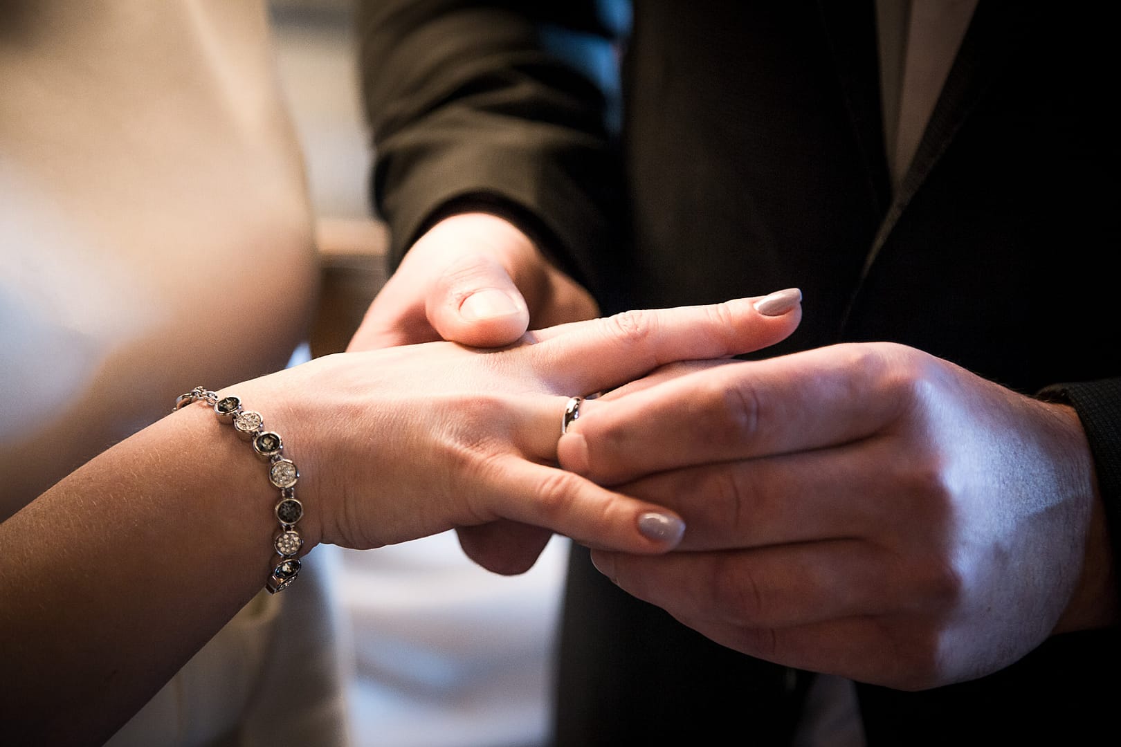 Bräutigams rechte Hand hält die rechte Hand der Braut fest, während er mit seiner linken Hand den Ehering über den Ringfinger der Braut anstecket.