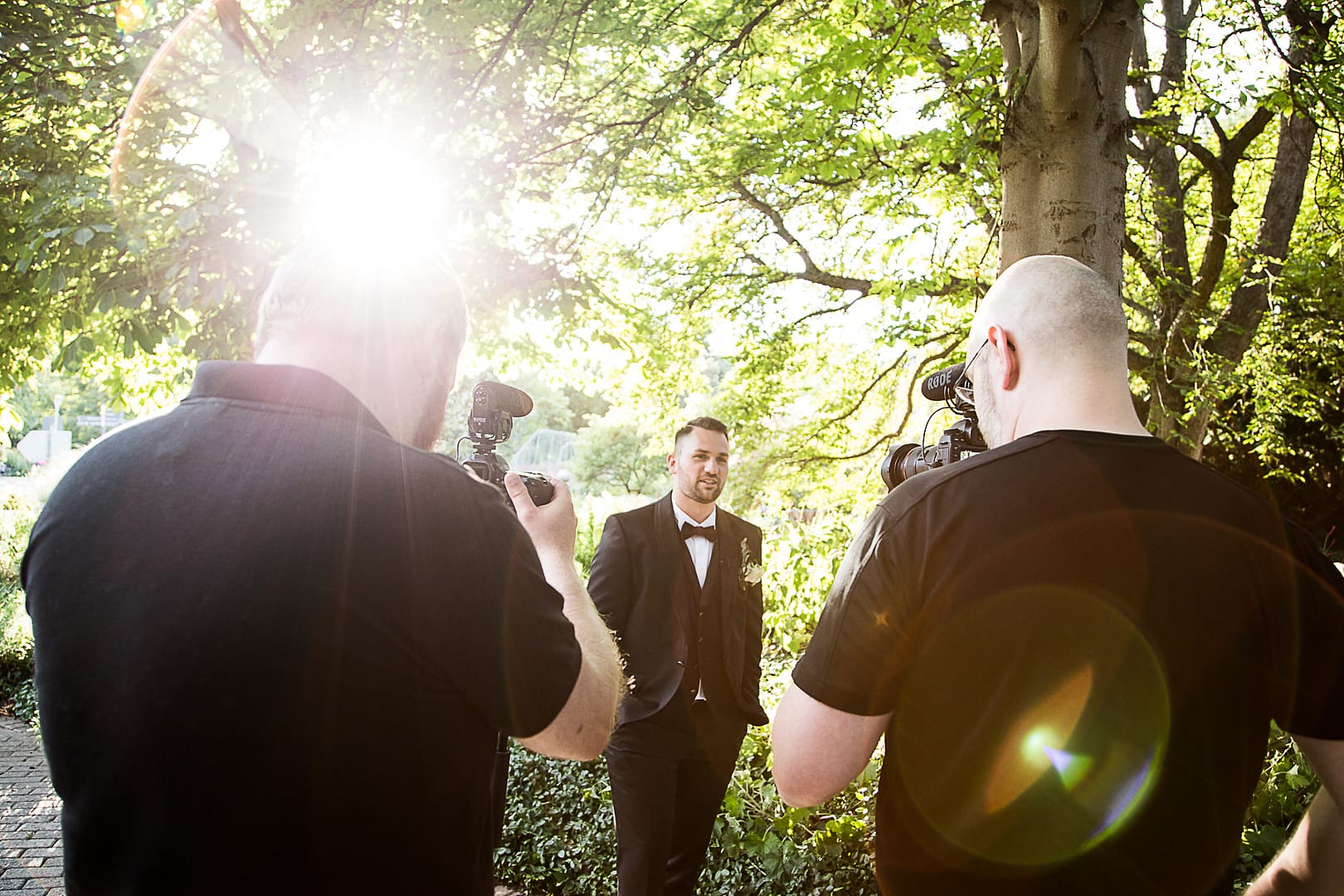 Der Bräutigam hält ein Interview für das Hochzeitsvideo im Garten der Location ab. Er wird hierbei von zwei Kameraleuten gefilmt.