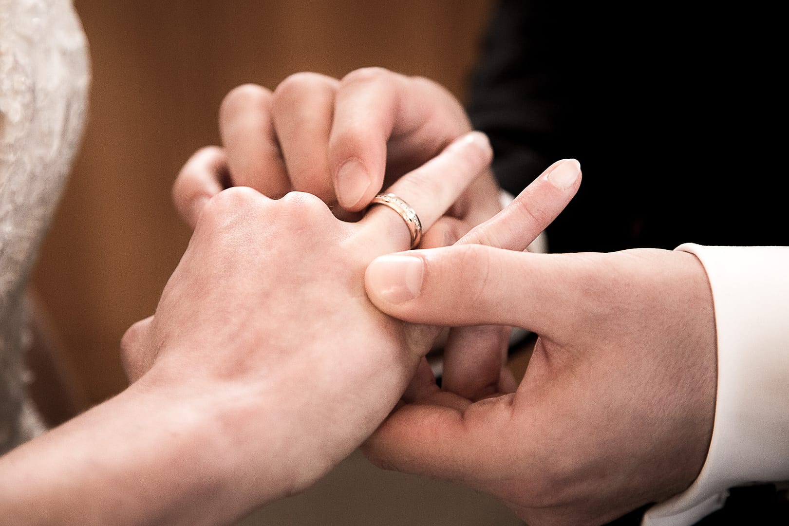 Eine Nahaufnahme der Hand von der Braut, während der Bräutigam den Ehering auf den Ringfinger der Braut aufsteckt.