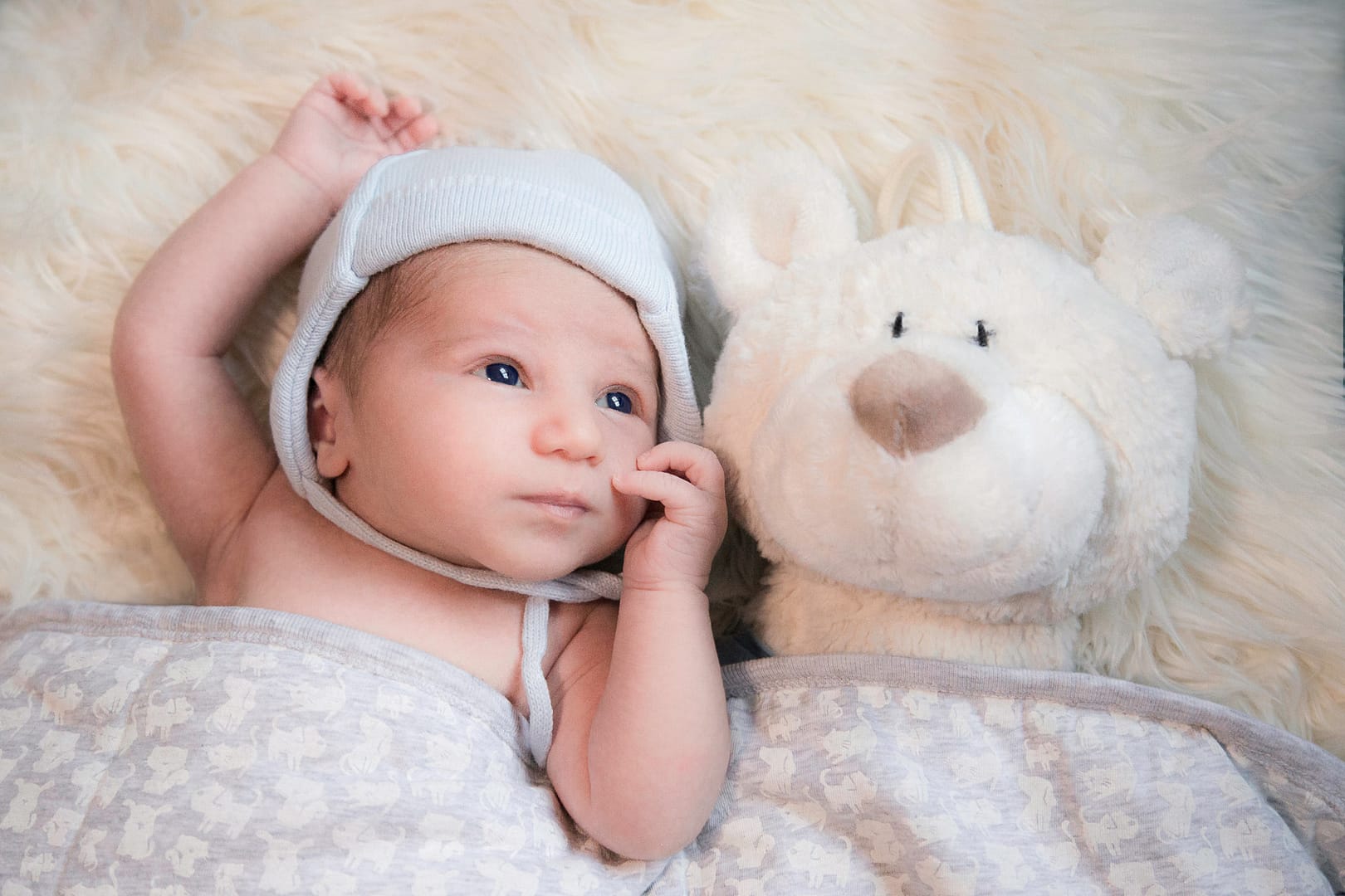 Neugeborenes Baby mit Babymütze im Bettchen mit Teddybät