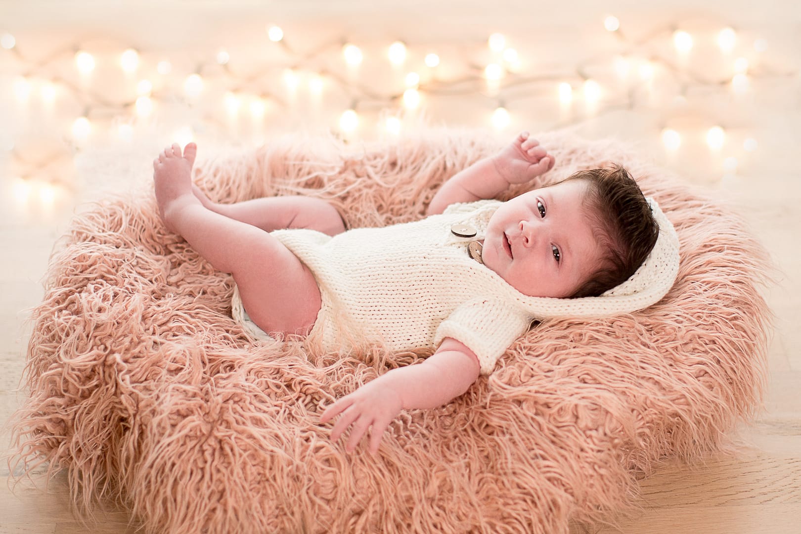 Baby im kuscheligen Fell mit Weihnachtslichterkette im Hintergrund
