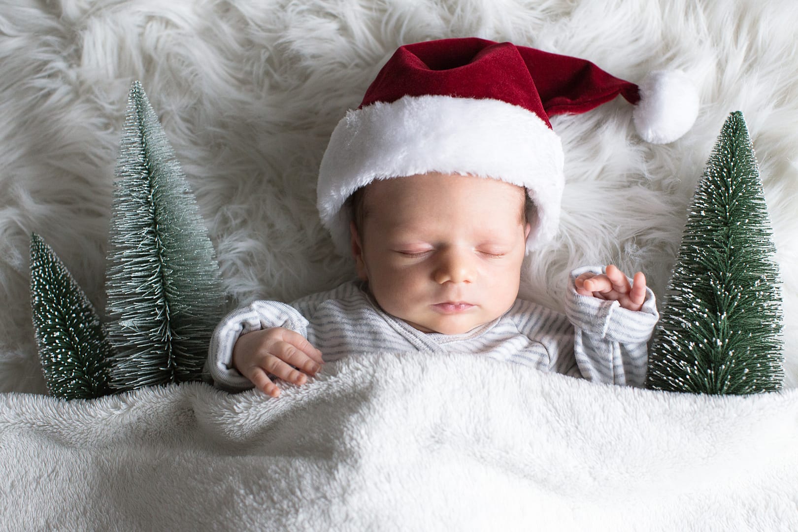 Schlafendes Baby im weihnachtlich dekoriertem Bett mit Weihnachtsmannmütze
