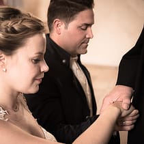 Das Traupaar kniet vor dem Priester nieder und legt dabei mit geschlossenen Augen seine rechte Hand übereinander. Auf ihren Händen liegt die Hand des Priesters.