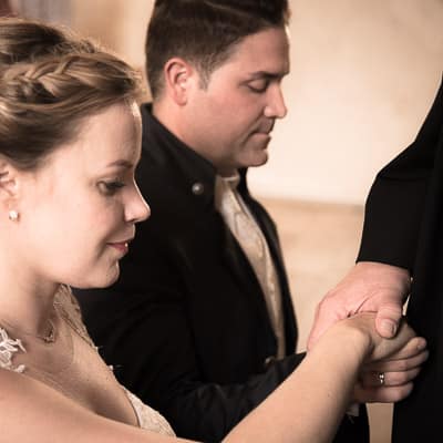 Das Traupaar kniet vor dem Priester nieder und legt dabei mit geschlossenen Augen seine rechte Hand übereinander. Auf ihren Händen liegt die Hand des Priesters.