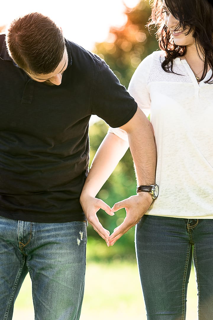 partner-fotoshooting: Ein Liebespaar steht nah bei Einander Schulter-an-Schulter und formt aus ihren Händen ein Herz.