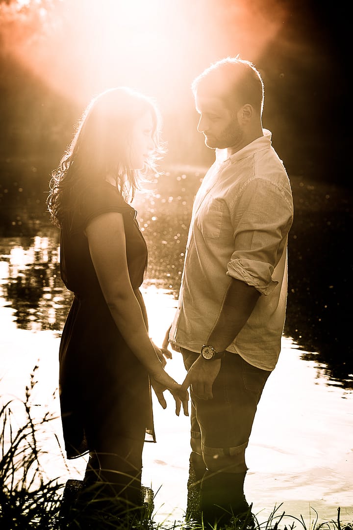partner-fotoshooting: Ein Liebespaar steht in einem See knietief. Sie berührend sich an den Händen und schauen sich verliebt in die Augen. Ihre Köpfe werden die Strahlen der untergehenden Sonne umhüllt.