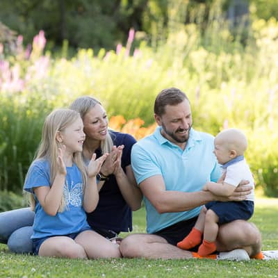 Fotograf Familienfotos: Familie mit Kleinkind sitzt auf einem Rasen im Park und klatscht mit Freude in die Hände