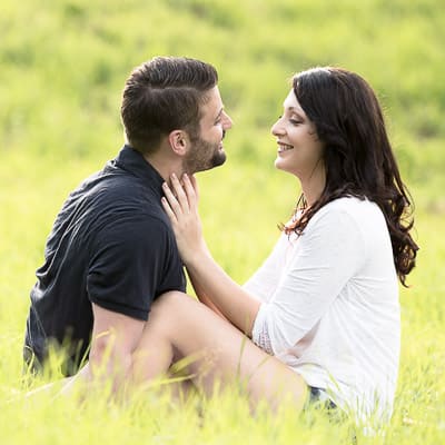 partner-fotoshooting: Ein Paar sitz im Feld und schaut sich mit verliebten Lächeln gegenseitig an.